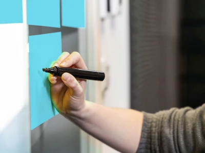 Klebezettel an einer Wand. Eine Hand mit einem Stift.