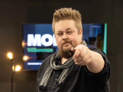 René hält einen Presenter in die Kamera