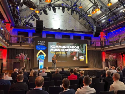 René auf einer Bühne. Auf der LED-Wand steht: Kommunikation muss begeistern.