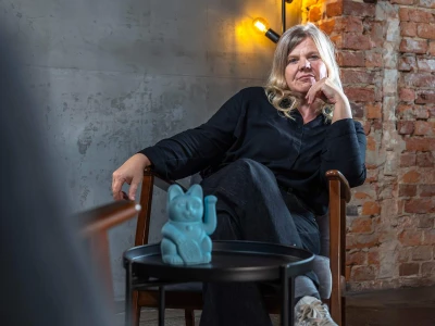 Christine sitzt auf einem Stuhl, vor ihr ein Beistelltisch mit blauer Winkekatze.