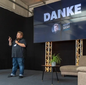 René auf einer Bühne. TV-Leinwand zeigt Danke-Schriftzug.