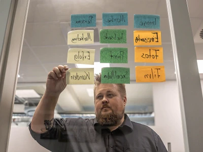 Klebezettel an einer Glaswand, René im Hintergrund und klebt Zettel.