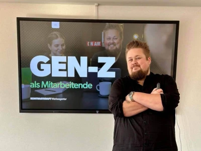 René vor einem TV mit der Präsentation Gen-Z als Mitarbeitende