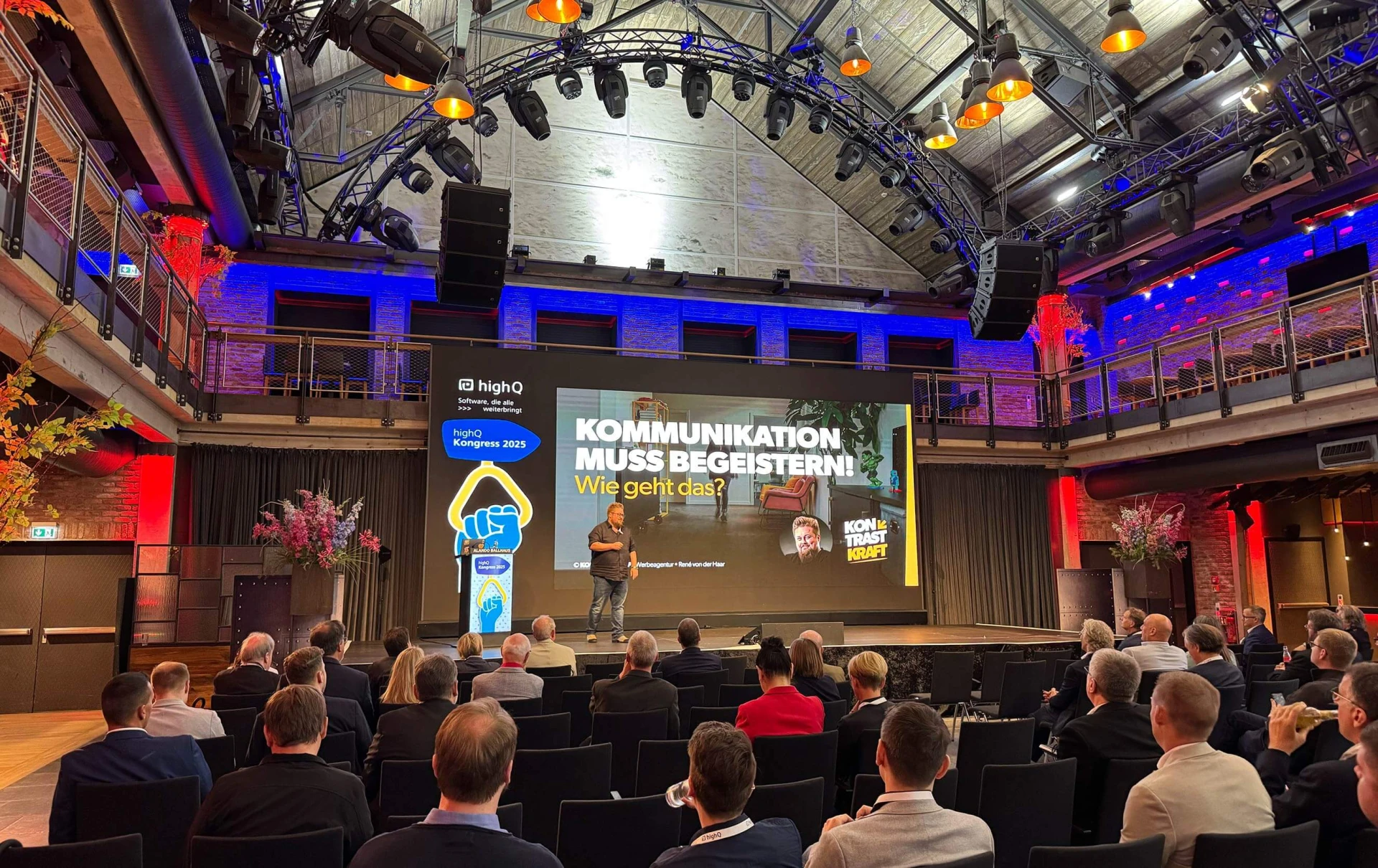 René auf einer Bühne. Auf der LED-Wand steht: Kommunikation muss begeistern.