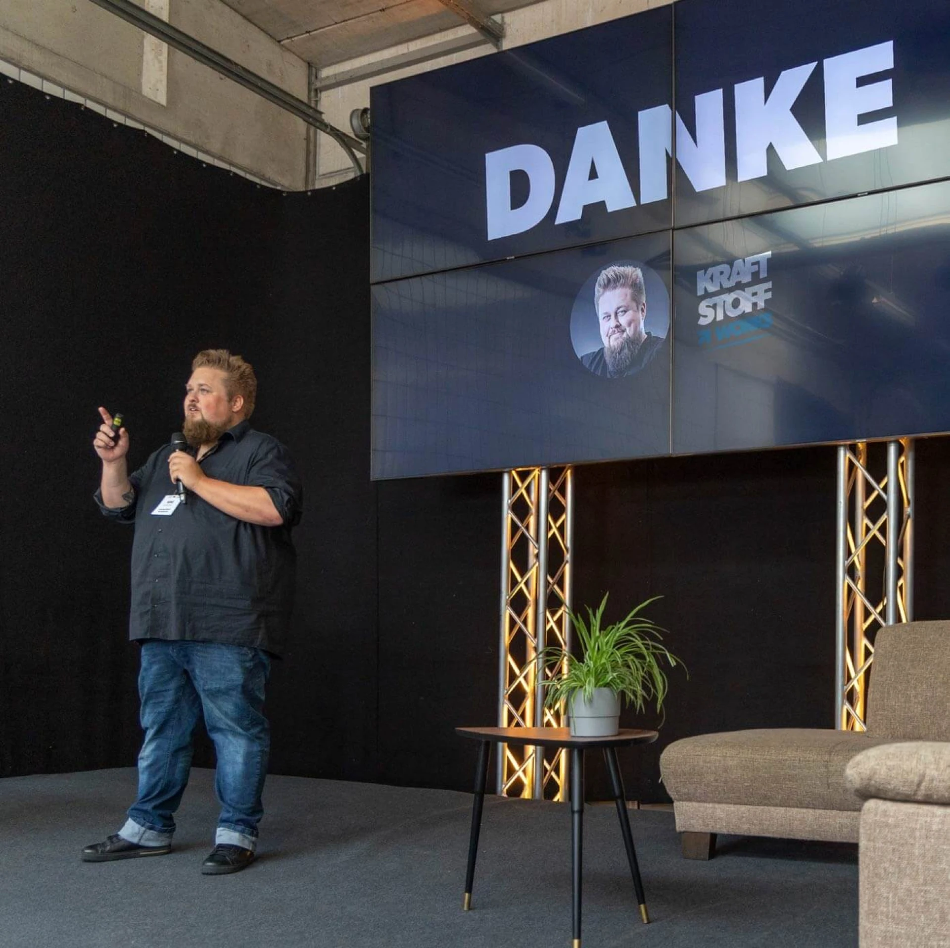 René auf einer Bühne. TV-Leinwand zeigt Danke-Schriftzug.