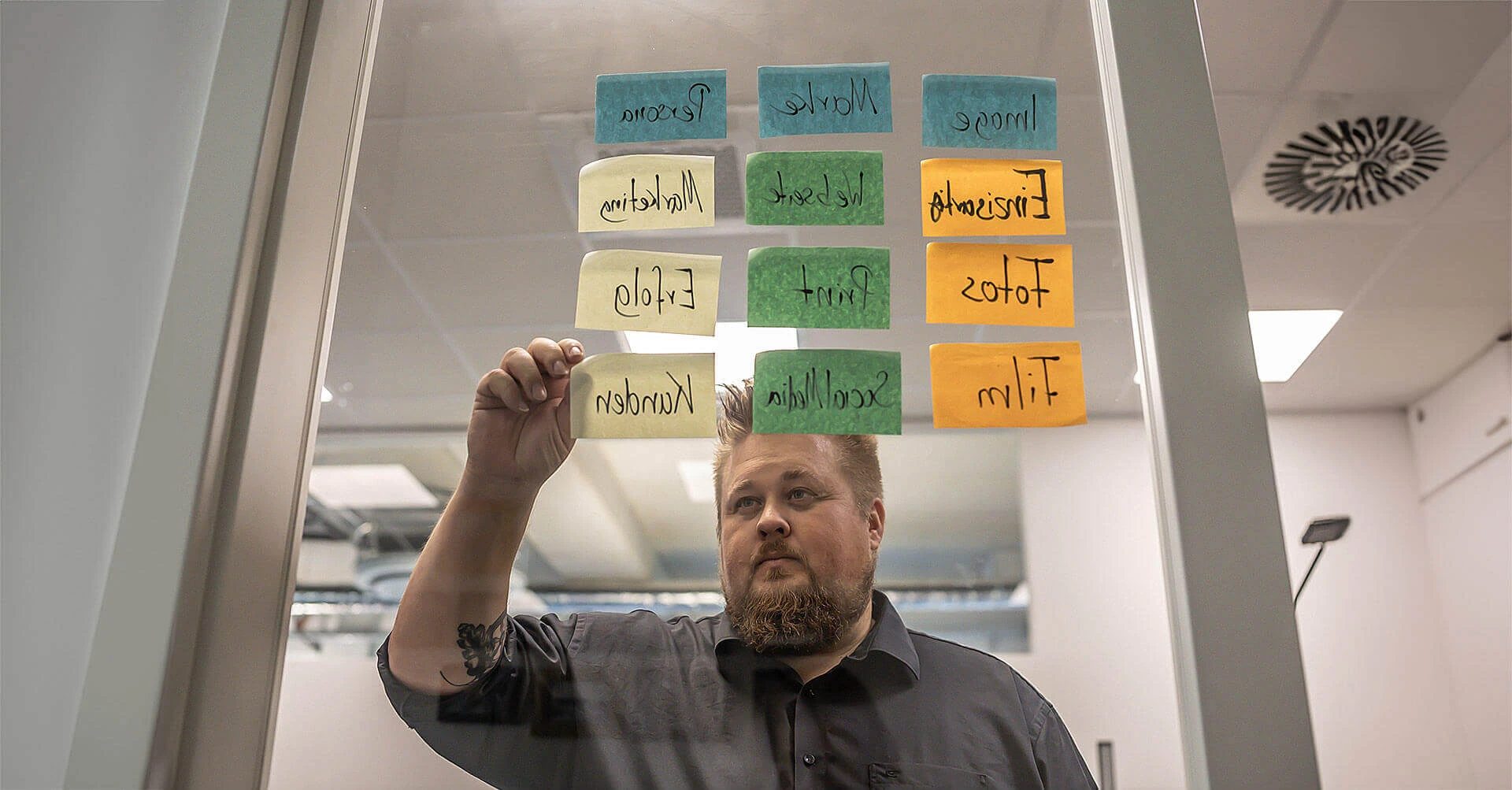 Klebezettel an einer Glaswand, René im Hintergrund und klebt Zettel.