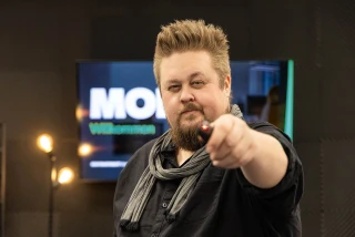 René hält einen Presenter in die Kamera