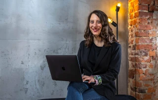 Kora sitzt auf einer Bank und schreibt auf einem Laptop