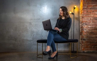 Kora sitzt auf einer Bank und schreibt auf einem Laptop