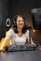 Foto von einer Frau mit Kopfhörern vor einem Podcastmirkofon, die in die Kamera lächelt.