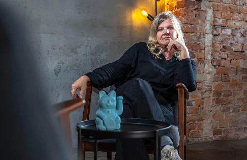 Christine sitzt auf einem Stuhl, vor ihr ein Beistelltisch mit blauer Winkekatze.