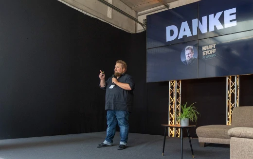 René auf einer Bühne. TV-Leinwand zeigt Danke-Schriftzug.